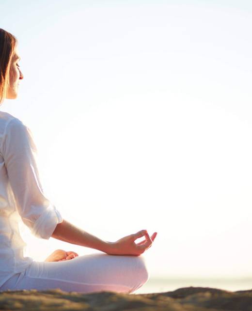 Side view of meditating woman sitting in pose of lotus against clear sky outdoors